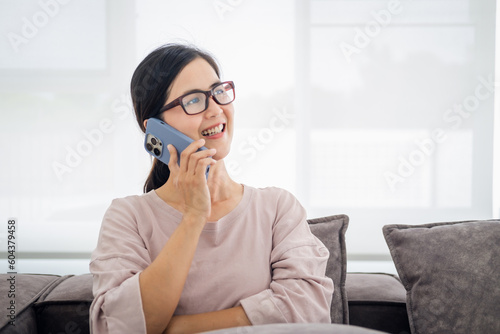 Happy stylish mature woman remote working from home distance office on laptop talking on phone . Smiling middle aged business lady using computer watching webinar sit on couch in living room. © Fahng