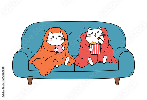 Two cats sitting on sofa wrapped in blanket and watching TV.