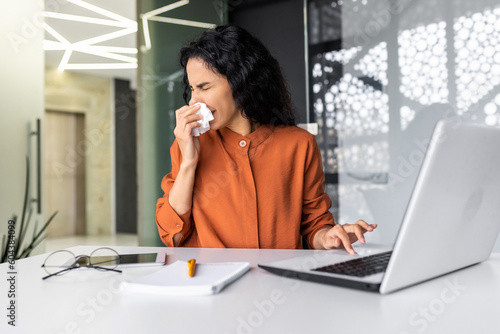 Tableau sur toile Young woman working sick at workplace inside office, worker sneezing has runny nose and allergy, hispanic sitting at table with laptop at work