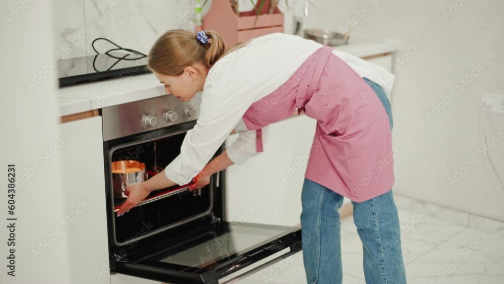 Confectioner woman in pink apron puts round metal ring with cheesecake in oven for baking. Confectioner woman in pink apron puts round metal ring with cheesecake in oven for baking.