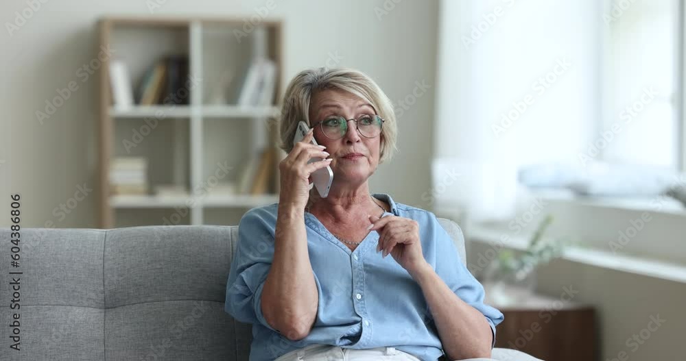 Serious concerned senior woman in glasses talking on mobile phone, speaking to client, doctor, support service hotline operator, telling problem, listening, making call from home couch Serious concerned senior woman in glasses talking on mobile phone, speaking to client, doctor, support service hotline operator, telling problem, listening, making call from home couch