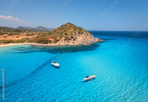 Aerial view of luxury yachts on blue sea at sunset in summer. Sardinia, Italy. Tropical seascape with speed boats, yachts, sea lagoon, mountain, ocean with transparent azure water, sky. Top drone view