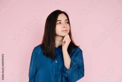 Serenity and Contemplation: Mindful Portrait of a Beautiful Girl with Hand on Chin, Gazing into Empty Space, Isolated on a Calming Pink Background