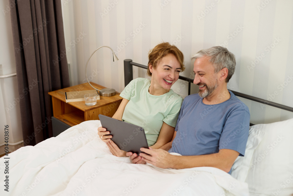 Smiling mature couple using digital tablet at home in bed Smiling mature couple using digital tablet at home in bed
