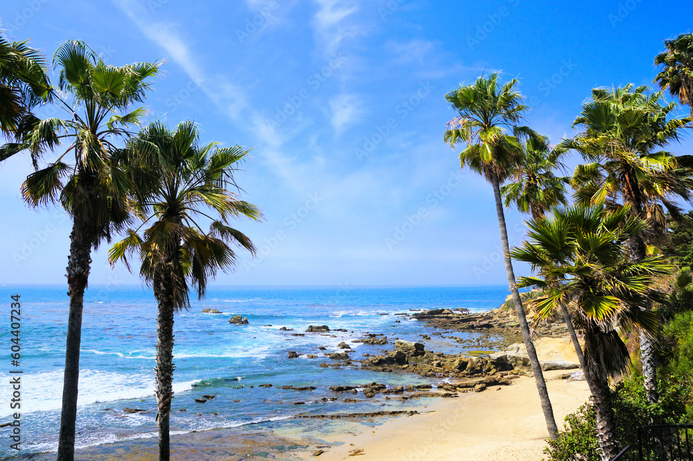Fototapeta premium Palm trees framing the sandy shores of the blue Pacific Ocean. Laguna Beach, California, USA.