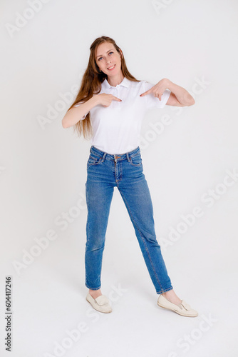 Cute and smiling Girl in a white t-shirt pointing down or at her t-shirt, smiling joyfully and expressing positive emotions on a white background.