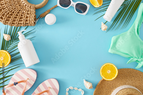 Concept of tropical beach vacation. Top view flat lay of swimsuit, flip-flops, sun-hat, sunscreen bottle, accessories, orange fruit and palm leaves on blue background with space for text or promotion