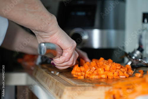 Hands only. Women are slicing carrots with a knife on a wooden board. High quality photo