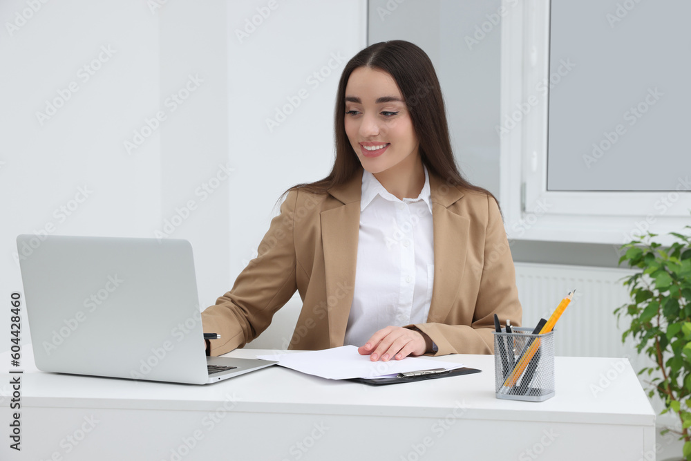 Young female intern working with laptop at table in office Young female intern working with laptop at table in office