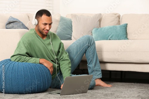 Smiling African American man in headphones with laptop near sofa at home