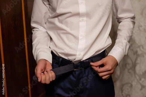 the groom fastens the leather belt on his trousers. the man gets dressed in the morning.