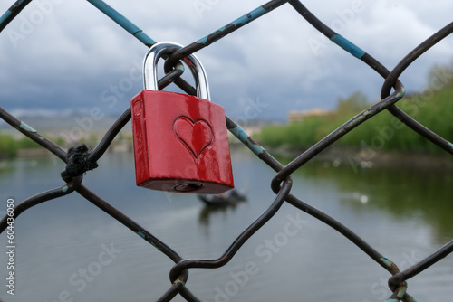 a lock with a red heart is hung on the wires, believing in love, a close-up red lock, selective focus