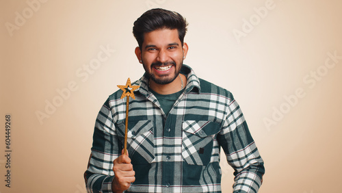 Magician wizard man gesturing with magic wand fairy stick, making wish come true, casting magician spell, advertising holidays sale discount. Handsome indian guy isolated on beige studio background