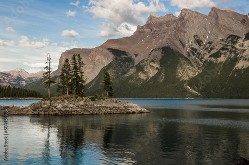 Lake Minnewanka, Banff National Park, Alberta, Canada, in summer - bue cloudy sky, mountains, small island in lake and calm clear spring water. concept - mountain tourism. copy space. 
