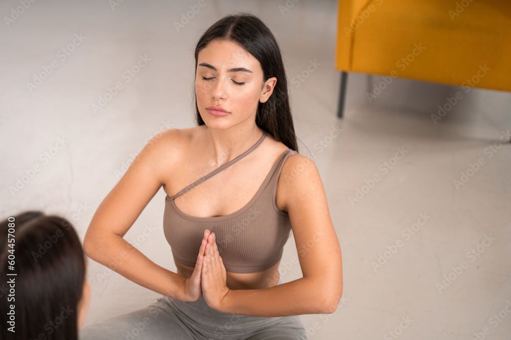 Peaceful young women practicing yoga with her sister, sitting on floor with legs Peaceful young women practicing yoga with her sister, sitting on floor with legs