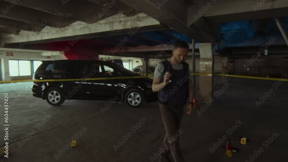 Full follow shot of Caucasian male police detective in bulletproof vest walking from car under yellow barrier tape towards corpse at crime scene, holding torch, lifting sheet and looking at body Full follow shot of Caucasian male police detective in bulletproof vest walking from car under yellow barrier tape towards corpse at crime scene, holding torch, lifting sheet and looking at body