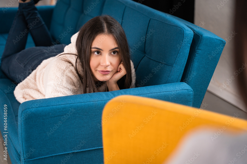 Serious brunette woman laying at the sofa and listening her bestie Serious brunette woman laying at the sofa and listening her bestie