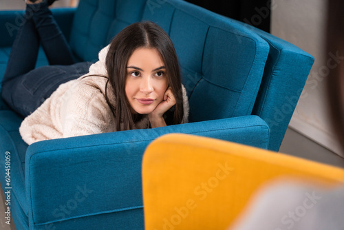 Serious brunette woman laying at the sofa and listening her bestie