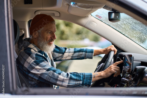 Older man sitting in camper van using gps navigation map system digital device. Smiling mature active traveler driving car vehicle looking at screen touching sensor gadget dashboard on the way.