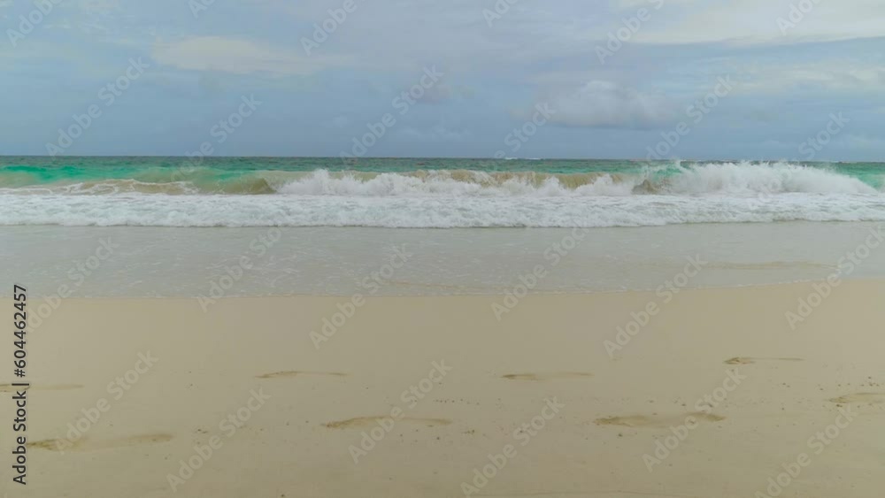Fresh ocean waves breaking in cloudy weather towards a beautiful sandy beach with footprints in the foreground. Cloudy sky before a storm. Stormy weather in ocean. Ocean and sky background landscape Fresh ocean waves breaking in cloudy weather towards a beautiful sandy beach with footprints in the foreground. Cloudy sky before a storm. Stormy weather in ocean. Ocean and sky background landscape