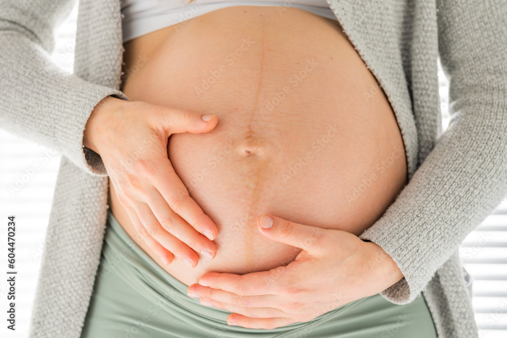Front view of midsection of unrecognizable woman gently massaging her belly in final months of pregnancy. Pregnancy first trimester - week 18. Front view. White background.