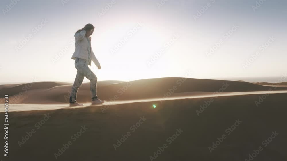 Happy hiker female on top of sandhill at scenic golden sunset with lens flare. Drone following caucasian woman on windy day in desert. Free female traveler walking by cinematic natural landscape 4K Happy hiker female on top of sandhill at scenic golden sunset with lens flare. Drone following caucasian woman on windy day in desert. Free female traveler walking by cinematic natural landscape 4K