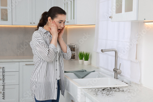 Shocked woman looking at affected with mold countertop in kitchen