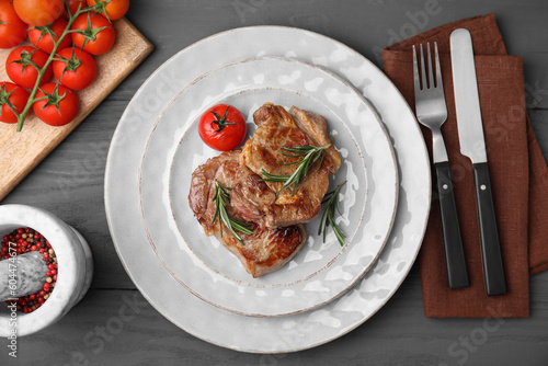 Delicious fried meat with rosemary and tomato served on grey wooden table, flat lay