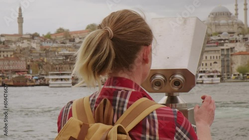 Woman tourist looking through binoculars at cityscape on observation deck.