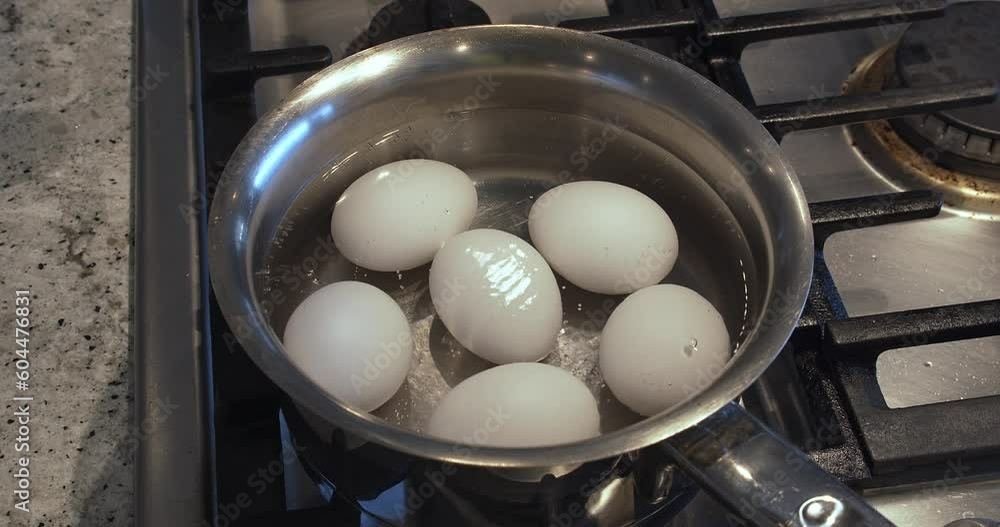 Eggs in boiling water to make boiled eggs. The water is gently simmering over low heat in a stainless steel pot with gas cooktop in a house kitchen Eggs in boiling water to make boiled eggs. The water is gently simmering over low heat in a stainless steel pot with gas cooktop in a house kitchen
