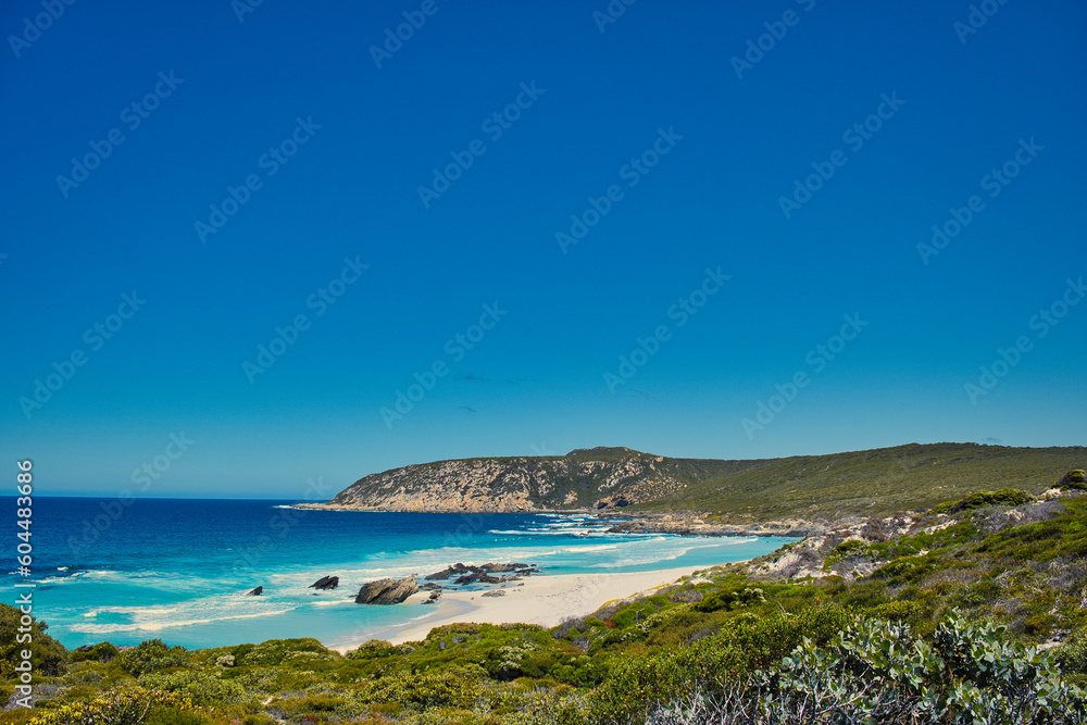 Azure blue sea, rocky hills and low coastal vegetation: West Beach, along the Hakea Trail in Fitzgerald River National Park, south coast of Western Australia.

