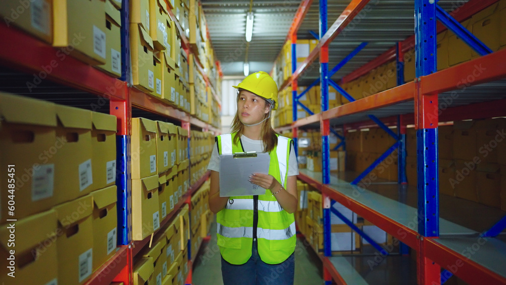Female engineer walking in warehouse store. She checking product in warehouse. Interior of cargo in ecommerce and logistic concept. Depot. People lifestyle. Shipment service.