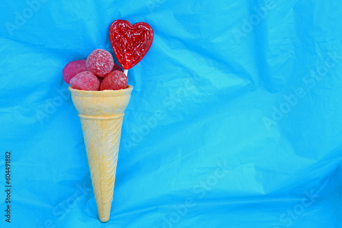 Horizontal side view of red gummies and heart candy inside of ice cream cone with bright blue background and copy space.