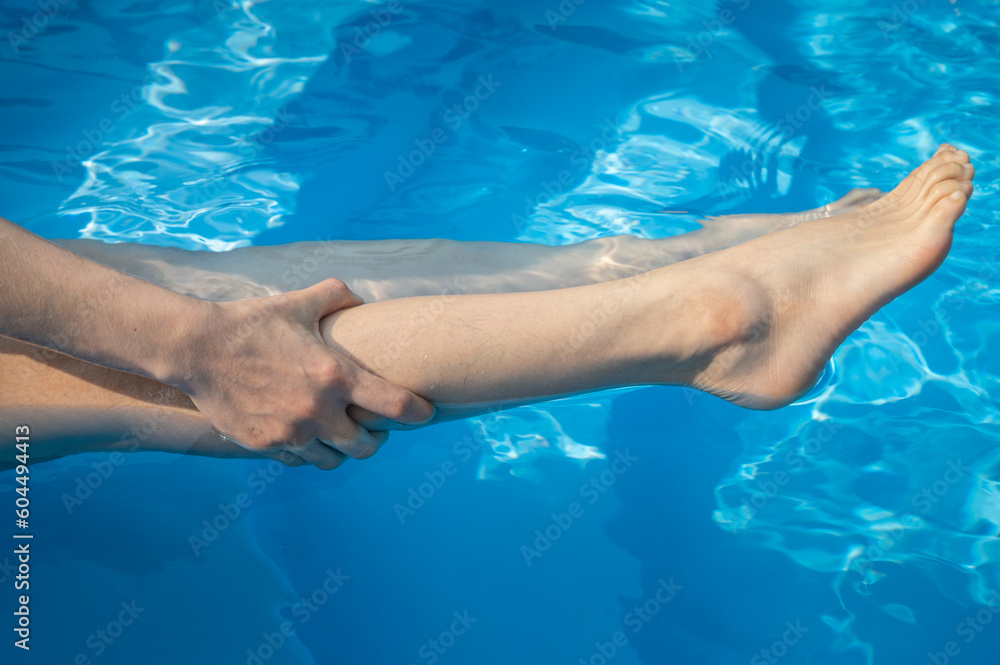 Close up of woman having cramp on her legs after swimming in swimming pool. To relieve muscle cramps during swimming, stretch, and massage cramped muscles and the surrounding area.