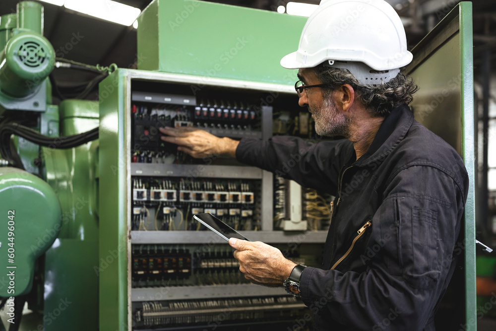 Electrical Engineer team working front control panel, An electrical engineer is installing and using a tablet to monitor the operation of an electrical control panel in a factory service room.