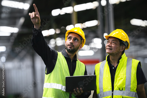 technician, supervisor with a senior foreman holding a walkie-talkie to command or inspect work with a checklist computer The background is an industrial warehouse.