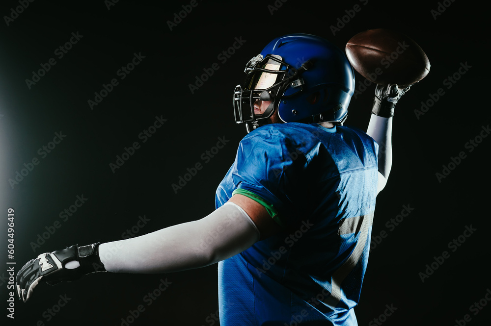 An Asian man with a red beard in a blue American football uniform throws a ball against a black background.