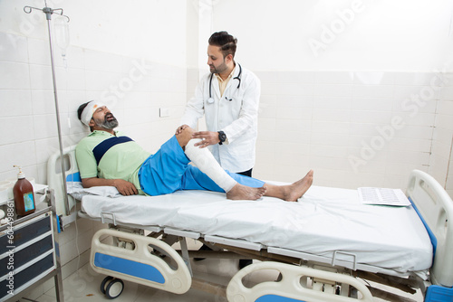 Indian orthopedic doctor examining patient with fractured leg lying on bed at hospital  healthcare concept.