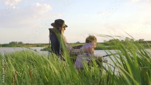 Grandfather, Grandson Go Fishing Together in evening at sunset time in summer day on river in countryside Grandpa kid Sitting On Bank Of River, Slow motion, Hobby Interests Lifestyle family traditions photo