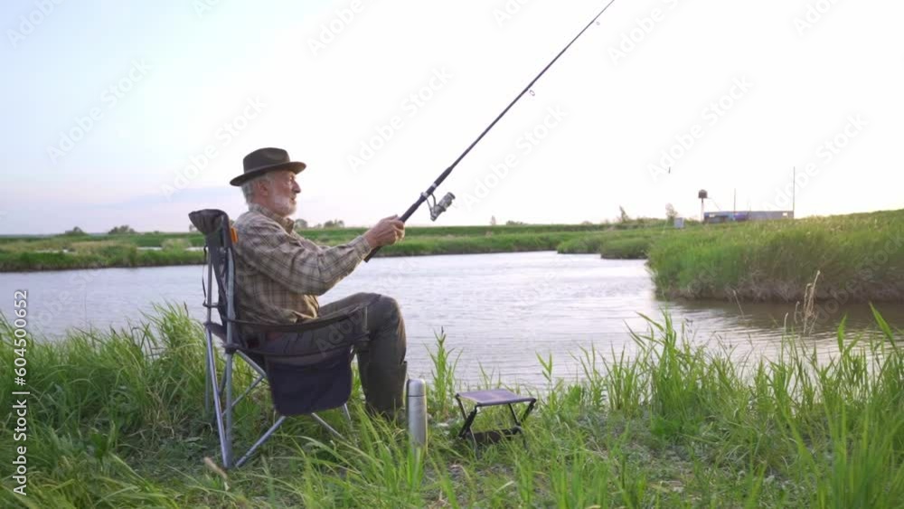 old grey-haired man catching fish. Retirement fishery, Slow motion. Senior man fishing in river, enjoying life. Fishing and sport concept. Side view on nice elderly man in casual wear enjoy fishing old grey-haired man catching fish. Retirement fishery, Slow motion. Senior man fishing in river, enjoying life. Fishing and sport concept. Side view on nice elderly man in casual wear enjoy fishing