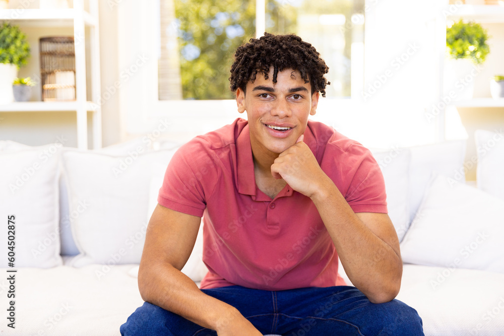 Portrait of biracial young man with hand on chin looking at camera while sitting on sofa Portrait of biracial young man with hand on chin looking at camera while sitting on sofa