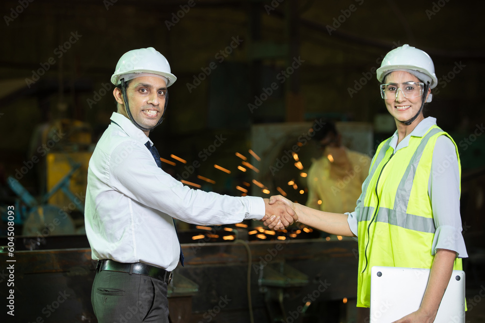 Two young male and female indian engineers wearing safety hard hat and vest do handshake at industrial factory. Two young male and female indian engineers wearing safety hard hat and vest do handshake at industrial factory.