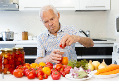 old gray haired man makes harvests for the winter pickles tomatoes