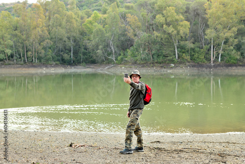 hombre adulto con una mochila roja haciendo fotos y shelfies en un bosque con un lago en Marbella España