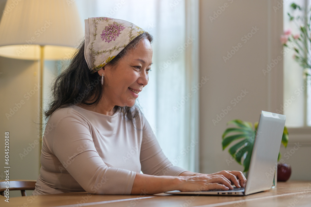 Pleasant mature woman using laptop while sitting at table and doing online shopping or chatting in social networks at home. Pleasant mature woman using laptop while sitting at table and doing online shopping or chatting in social networks at home.