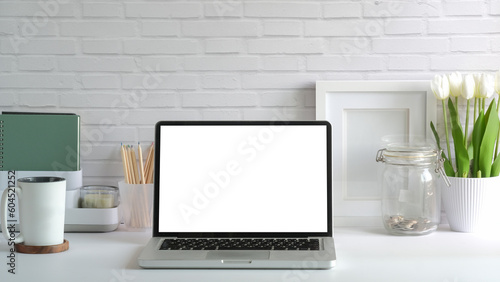 Front view of laptop computer, coffee cup and potted plant on white table. Empty screen for your advertise design..