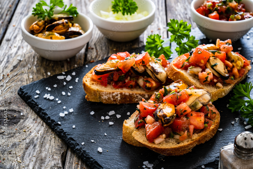 Tasty sandwiches - toasted bread with tomatoes and mussels on wooden table
