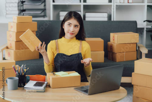 tarting Small business entrepreneur SME freelance,Portrait young woman working at home office, BOX,smartphone,laptop, online, marketing, packaging, delivery, SME, e-commerce concept © Kritdanai