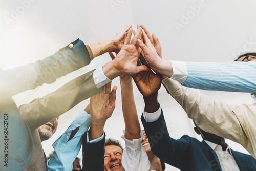 Low-angle shot of a diverse team of colleagues in a bright office. They are standing together, giving a group high five. The focus is on the hands, with light flares entering the lens photo