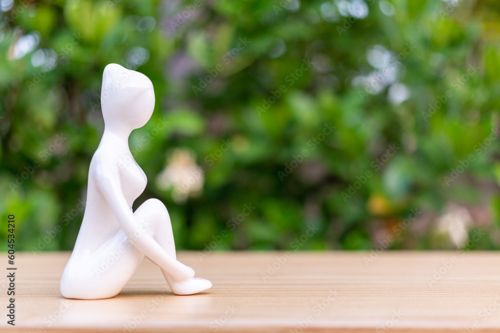 Ceramic Yoga Figurine of Woman doing yoga pose on wooden floor and green leaf background Ceramic Yoga Figurine of Woman doing yoga pose on wooden floor and green leaf background